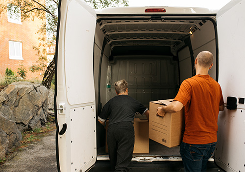 Family members placing moving boxes inside a rented cargo van as part of a self-managed move in Portugal.