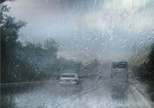 Vista de dentro do carro, através do para-brisas com chuva intensa, com trânsito à frente