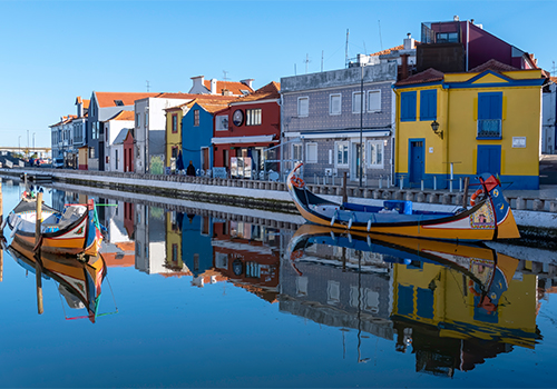 Vista do canal da Ria de Aveiro com barcos moliceiros e edifícios coloridos no centro histórico da cidade.