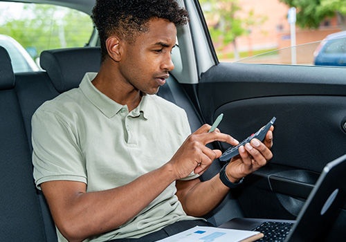 Driver inside a car using a calculator and smartphone to calculate fuel cost for a trip.