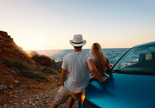 Couple on the roadside enjoying the sea, leaning against the car.