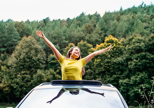 Mulher de braços abertos, a sair pelo teto panorâmico do carro