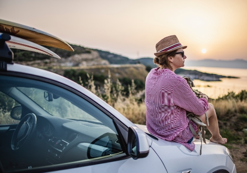 Jovem expat em Portugal, sentada em cima de um carro alugado, a assistir ao pôr-do-sol.