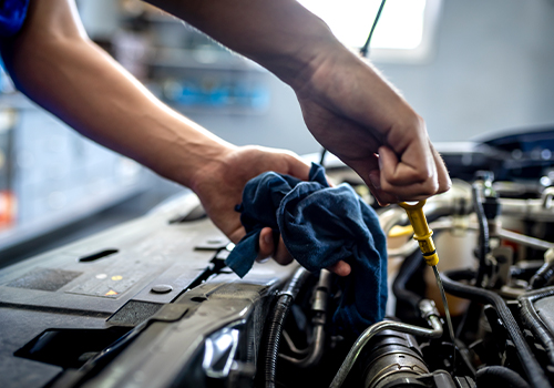 Mechanic checking the engine oil level during car maintenance before a vehicle inspection.