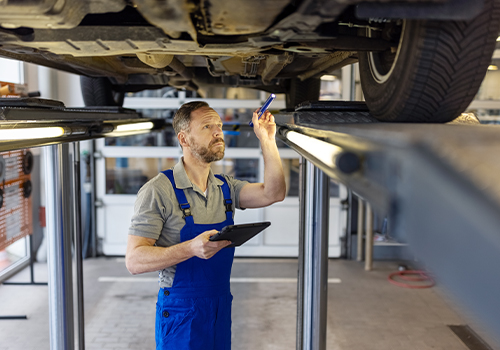 Technician inspecting a car raised on a vehicle lift during a mandatory periodic inspection.
