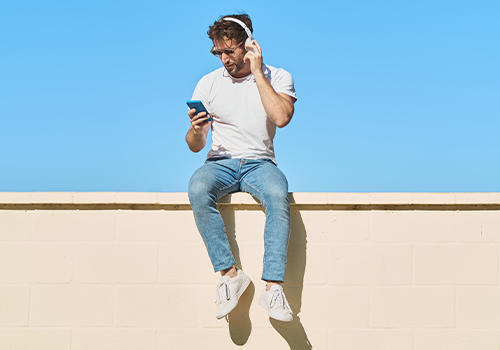 Man with headphones sitting on a wall