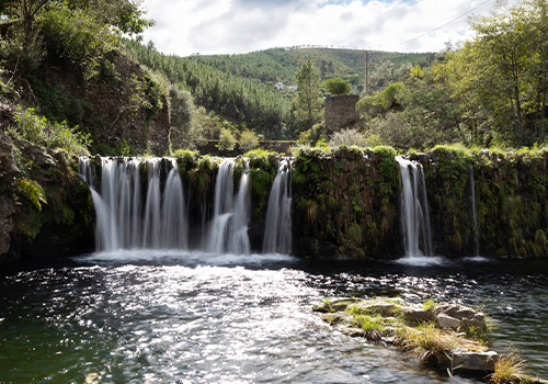 Cascata rodeada por vegetação e montanhas na Serra da Estrela, um dos destinos mais refrescantes para o verão em Portugal.