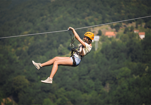 Woman riding a zip line at Pena Aventura Park with green mountains in the background.