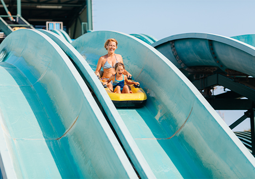 Mother and daughter sliding down a water slide at an amusement park on a summer day.