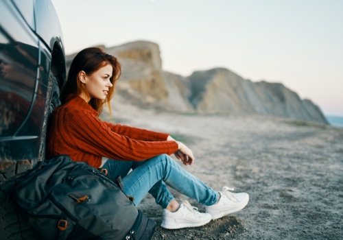 Mulher sentada no chão encostada ao carro na natureza